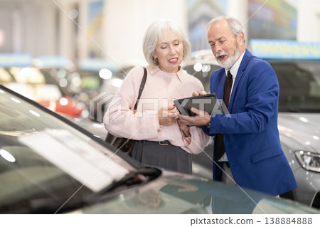 Senior salesman at car dealership offers to buy car to an elderly woman - demonstrating the best models of car dealership 138884888