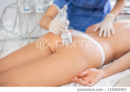 Aesthetician administering ice hammer therapy on female client buttocks 138884963
