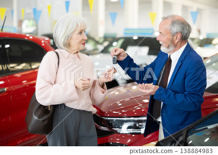 Elderly salesman handing car keys to woman at dealership 138884983