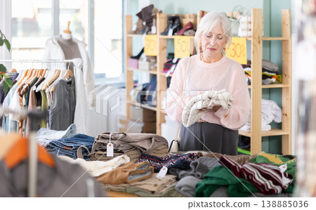 Elderly woman chooses sweater in clothing store Elderly woman chooses sweater in clothing store 138885036