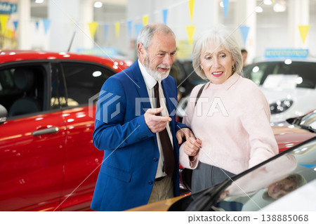 salesman shows a car to an elderly woman at a car dealership salesman shows a car to an elderly woman at a car dealership 138885068