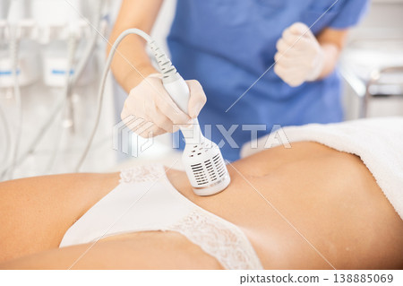 Aesthetician administering cold hammer therapy on female client belly Aesthetician administering cold hammer therapy on female client belly 138885069