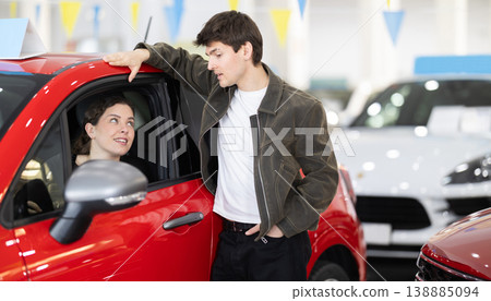 Young couple in a car dealership chooses a car Young couple in a car dealership chooses a car 138885094