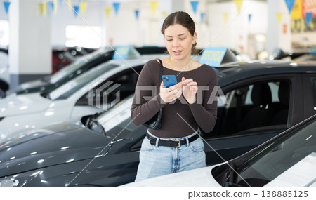 Young woman scanning QR code while choosing car at dealership Young woman scanning QR code while choosing car at dealership 138885125
