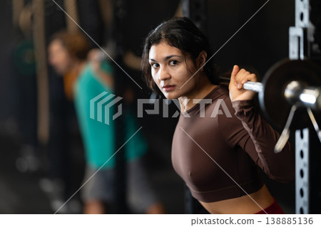 Sportive Latina girl lifting barbell in sports hall 138885136