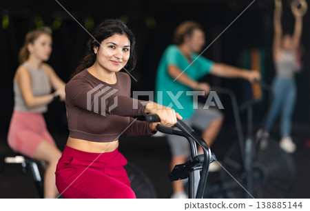 Latina woman doing exercises on air bike in Crossfit gym Latina woman doing exercises on air bike in Crossfit gym 138885144