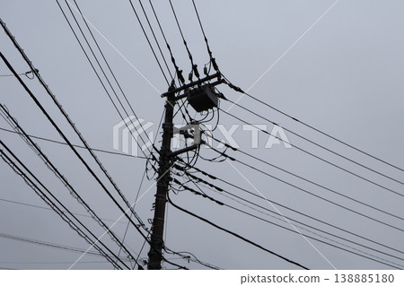 A scene from a Japanese residential area on a cloudy day, with utility poles and a complex network of power lines. 138885180