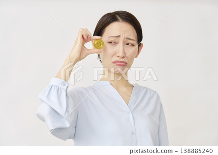 A woman in her 40s holding Bitcoin with a troubled look on her face, white background 138885240