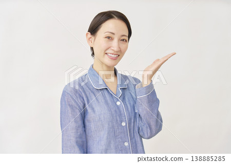 A woman in pajamas pointing to the right with her palm on a white background 138885285