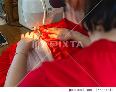 Sewing a red dress at a home sewing station in the afternoon Sewing a red dress at a home sewing station in the afternoon 138885818