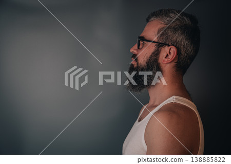Man with beard is standing in profile against a plain wall Man with beard is standing in profile against a plain wall 138885822