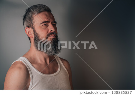 Man looking to the side with a beard and gray hair in simple clothing Man looking to the side with a beard and gray hair in simple clothing 138885827