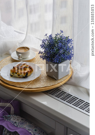Coffee and pastry on a tray near a window with a flower pot Coffee and pastry on a tray near a window with a flower pot 138885853