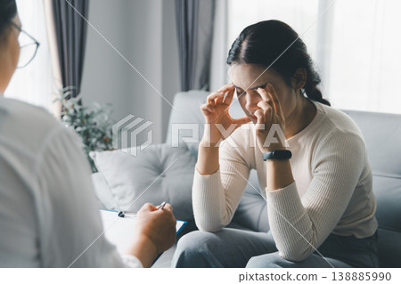 Mental health counseling concept with stressed woman touching temples during therapy session at home, showing anxiety, emotional pressure, therapist support, coping, trust and psychological care. Mental health counseling concept with stressed woman touching temples during therapy session at home, showing anxiety, emotional pressure, therapist support, coping, trust and psychological care. 138885990