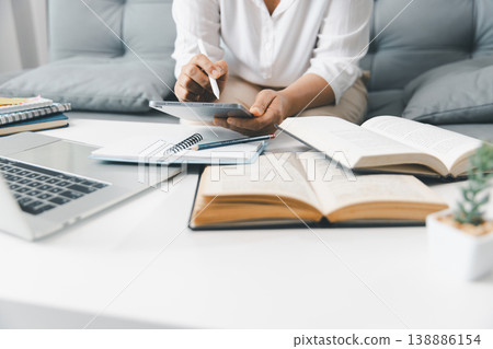 Hands using tablet with stylus beside laptop and open textbooks on white desk, taking notes for online learning, homework and exam prep in bright modern home study workspace. study, learning, homework Hands using tablet with stylus beside laptop and open textbooks on white desk, taking notes for online learning, homework and exam prep in bright modern home study workspace. study, learning, homework 138886154