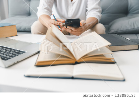 Hands studying at home with open textbook, laptop and smartphone, taking notes with pencil at bright white desk. Online learning, research and exam preparation concept for students and education. Hands studying at home with open textbook, laptop and smartphone, taking notes with pencil at bright white desk. Online learning, research and exam preparation concept for students and education. 138886155