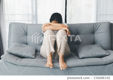 Depressed woman curled up on gray sofa, head down on arms, barefoot at home by bright window. Mental health anxiety, sadness, burnout, loneliness concept, copy space for therapy awareness. depressed Depressed woman curled up on gray sofa, head down on arms, barefoot at home by bright window. Mental health anxiety, sadness, burnout, loneliness concept, copy space for therapy awareness. depressed 138886192