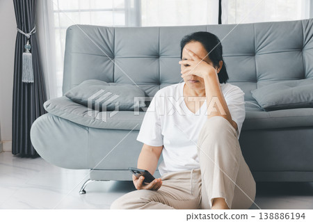 Depressed woman sitting on floor by gray sofa, hand on face, holding smartphone at home. Mental health anxiety, burnout and loneliness concept for therapy, support, awareness, copy space. depressed Depressed woman sitting on floor by gray sofa, hand on face, holding smartphone at home. Mental health anxiety, burnout and loneliness concept for therapy, support, awareness, copy space. depressed 138886194