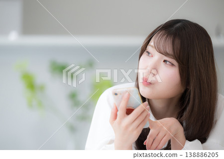 一張輕鬆的日常照片,照片中一位女性面朝下躺在家中,看著她的智慧型手機。 一張輕鬆的日常照片,照片中一位女性面朝下躺在家中,看著她的智慧型手機。 138886205