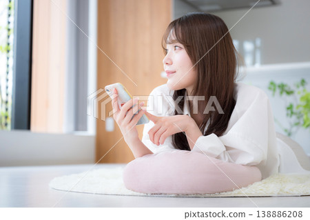 A woman relaxing at home, lying face down and looking at her smartphone. 138886208