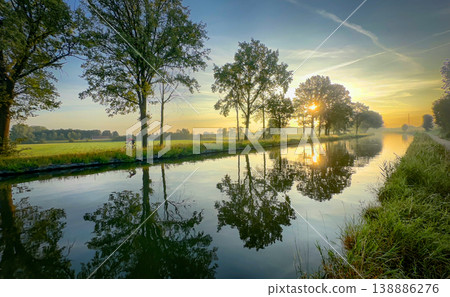 A colorful sunrise reflection over a tranquil canal captivates viewers with beauty and harmony A colorful sunrise reflection over a tranquil canal captivates viewers with beauty and harmony 138886276