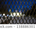 View of a building through a wire fence at night with blurred lights creating a unique scene 138886301