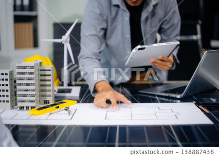 Engineer using compass on building plan with laptop, model, and wind turbine. Ideal for clean energy, architecture, 138887438