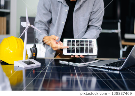 Engineer using tablet near solar panel and wind turbine model, representing clean energy, green innovation, and smart technology Engineer using tablet near solar panel and wind turbine model, representing clean energy, green innovation, and smart technology 138887469