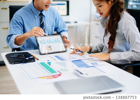 Two professionals reviewing business charts and data with tablet and documents. Ideal for financial planning, corporate teamwork, and modern office 138887753