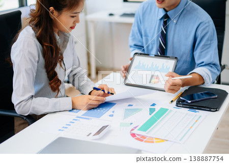 Two professionals reviewing business charts and data with tablet and documents. Ideal for financial planning, corporate teamwork, and modern office 138887754