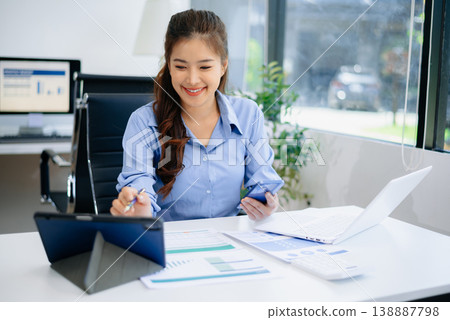 Asian woman in office working on business reports using laptop and documents. Perfect for finance, career, analysis, and modern professional lifestyle concepts. 138887798