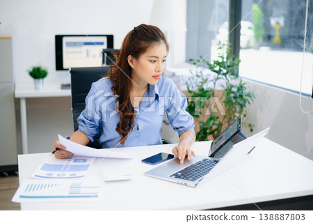 Young beautiful woman typing on tablet and laptop while sitting at the working white table 138887803