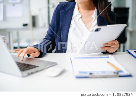 Confident Asian businesswoman working in modern office, using laptop and tablet, planning strategy at desk Confident Asian businesswoman working in modern office, using laptop and tablet, planning strategy at desk 138887924