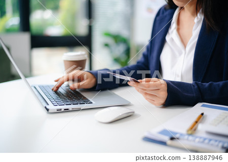 Closeup of smiling Asian businesswoman holding smartphone and credit card for online payment at office desk. Closeup of smiling Asian businesswoman holding smartphone and credit card for online payment at office desk. 138887946