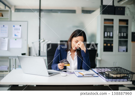 Stressed Asian businesswoman holding multiple credit cards in office, facing financial pressure. Stressed Asian businesswoman holding multiple credit cards in office, facing financial pressure. 138887960