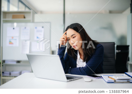 Asian businesswoman showing stress and frustration at office desk with laptop and calculator. Real people, financial pressure, work overload, deadline stress, burnout concept. Asian businesswoman showing stress and frustration at office desk with laptop and calculator. Real people, financial pressure, work overload, deadline stress, burnout concept. 138887964