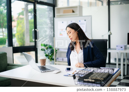 Asian businesswoman stretching arms in office with tired expression, relieving muscle tension from long work hours. Asian businesswoman stretching arms in office with tired expression, relieving muscle tension from long work hours. 138887973