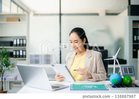 Asian woman holding smartphone and pen near globe, wind turbine, and solar panel on desk. Concept of clean energy, green business, carbon reduction, and smart communication. Asian woman holding smartphone and pen near globe, wind turbine, and solar panel on desk. Concept of clean energy, green business, carbon reduction, and smart communication. 138887987