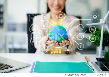 Hands holding Earth globe with futuristic clean energy icons overlay. Sustainability, smart technology, battery, wind, solar, and eco-friendly innovation concept in office. Hands holding Earth globe with futuristic clean energy icons overlay. Sustainability, smart technology, battery, wind, solar, and eco-friendly innovation concept in office. 138887994