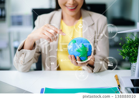 Hands holding Earth globe with futuristic clean energy icons overlay. Sustainability, smart technology, battery, wind, solar, and eco-friendly innovation concept in office. 138888010