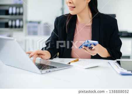 Confident Asian businesswoman using tablet in modern office with laptop and documents, showcasing finance, remote work 138888032