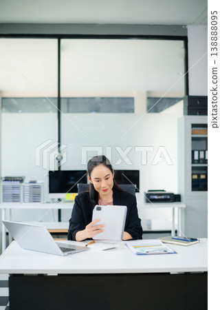 Smiling Asian businesswoman texting on phone at modern office desk with laptop, coffee, and documents Smiling Asian businesswoman texting on phone at modern office desk with laptop, coffee, and documents 138888095