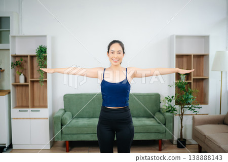 Young woman practices yoga and stretching with gym props on mat in modern home. Healthy lifestyle, wellness, motivation, balance, and indoor fitness activity. Young woman practices yoga and stretching with gym props on mat in modern home. Healthy lifestyle, wellness, motivation, balance, and indoor fitness activity. 138888143
