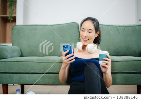Fit woman in athleisure sits on yoga mat with tablet, headphones, and workout gear. Modern indoor wellness, healthy lifestyle, and digital fitness at home. Fit woman in athleisure sits on yoga mat with tablet, headphones, and workout gear. Modern indoor wellness, healthy lifestyle, and digital fitness at home. 138888146