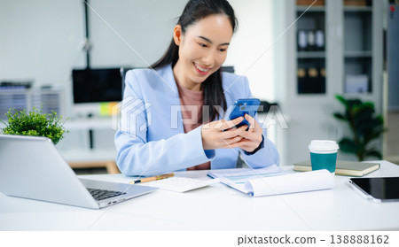 Asian businesswoman in blue blazer using tablet at modern office desk with laptop, coffee Asian businesswoman in blue blazer using tablet at modern office desk with laptop, coffee 138888162