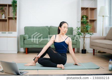Young Asian woman practicing yoga indoors on a mat. Calm, healthy lifestyle, stretching, wellness and fitness at home 138888218