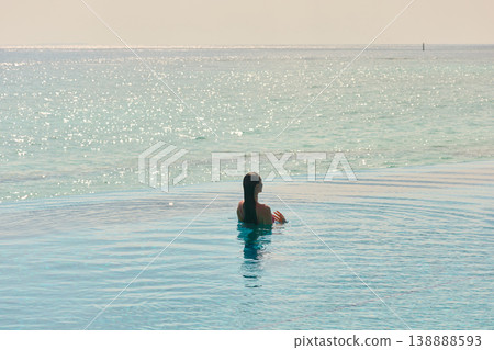 A beautiful tanned girl with an athletic physique in a swimsuit is at the edge of the pool of the villa pool on a sunset in the Maldives, she is happy and posing A beautiful tanned girl with an athletic physique in a swimsuit is at the edge of the pool of the villa pool on a sunset in the Maldives, she is happy and posing 138888593