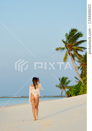 A beautiful tanned girl in a swimsuit walks along a white beach at sunset in the Maldives, she is happy, posing for a photographer A beautiful tanned girl in a swimsuit walks along a white beach at sunset in the Maldives, she is happy, posing for a photographer 138888603