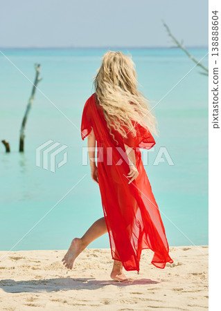 A beautiful tanned girl is wearing in red cape fun on the personal beach of the villa on a sunny day in the Maldives, she is happy and posing 138888604