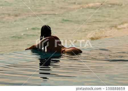 A beautiful tanned girl with an athletic physique in a swimsuit is at the edge of the pool of the villa pool on a sunset in the Maldives, she is happy and posing A beautiful tanned girl with an athletic physique in a swimsuit is at the edge of the pool of the villa pool on a sunset in the Maldives, she is happy and posing 138888659